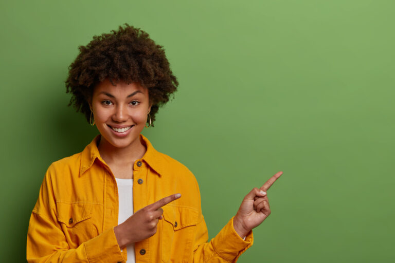 lovely-dark-skinned-woman-with-afro-hair-points-fore-fingers-right-suggests-going-this-direction-demonstrates-awesome-product-wears-yellow-jacket
